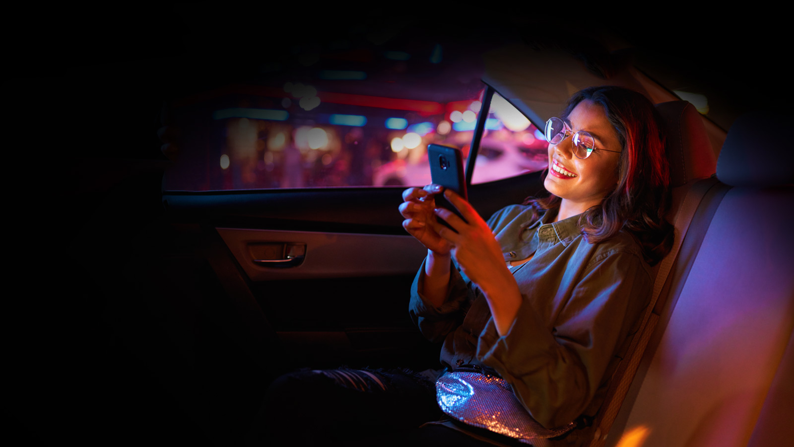 Mujer viajando en la parte de atrás de un auto mientras mira su celular
