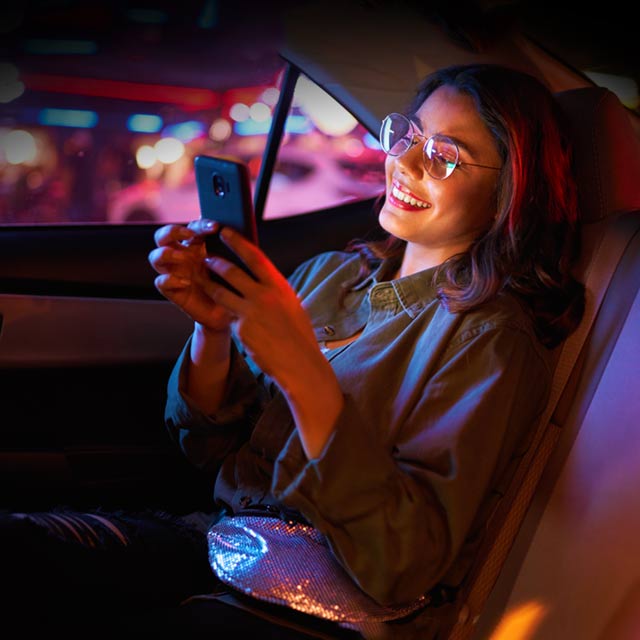 Mujer viajando en la parte de atrás de un auto mientras mira su celular